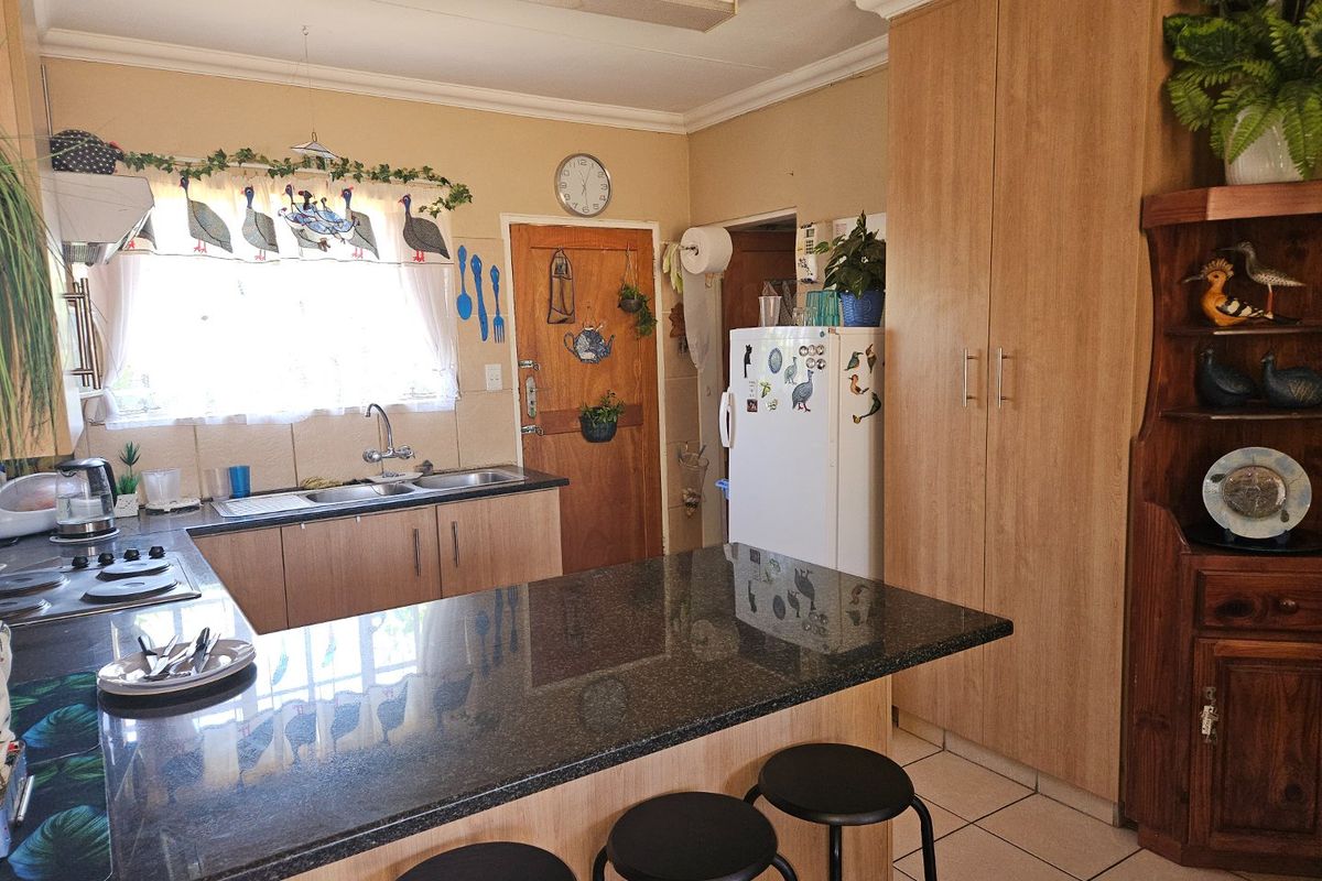 A functional kitchen featuring granite countertops, ample built-in cabinetry, a double sink, and a hob, with tiled flooring throughout.