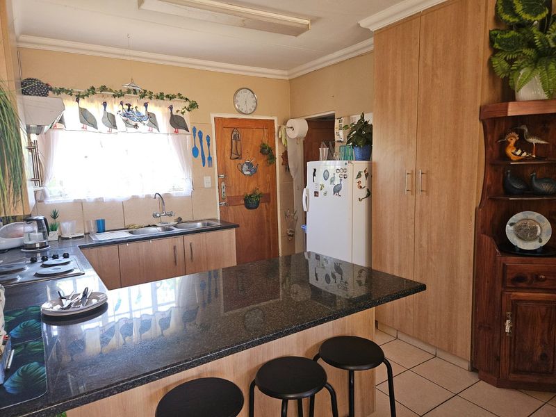 A functional kitchen featuring granite countertops, ample built-in cabinetry, a double sink, and a hob, with tiled flooring throughout.