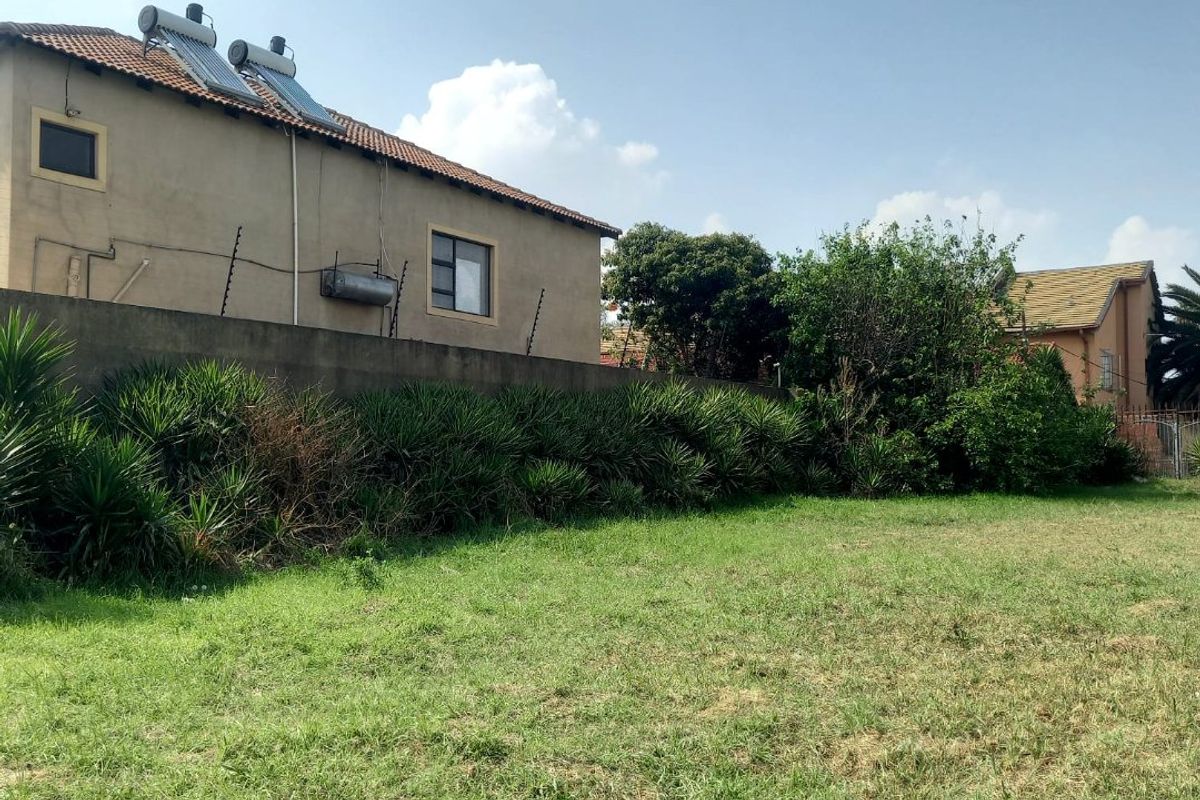 A view of the rear yard featuring a grass lawn, boundary wall with electric fencing, and a house with a solar water heating system.