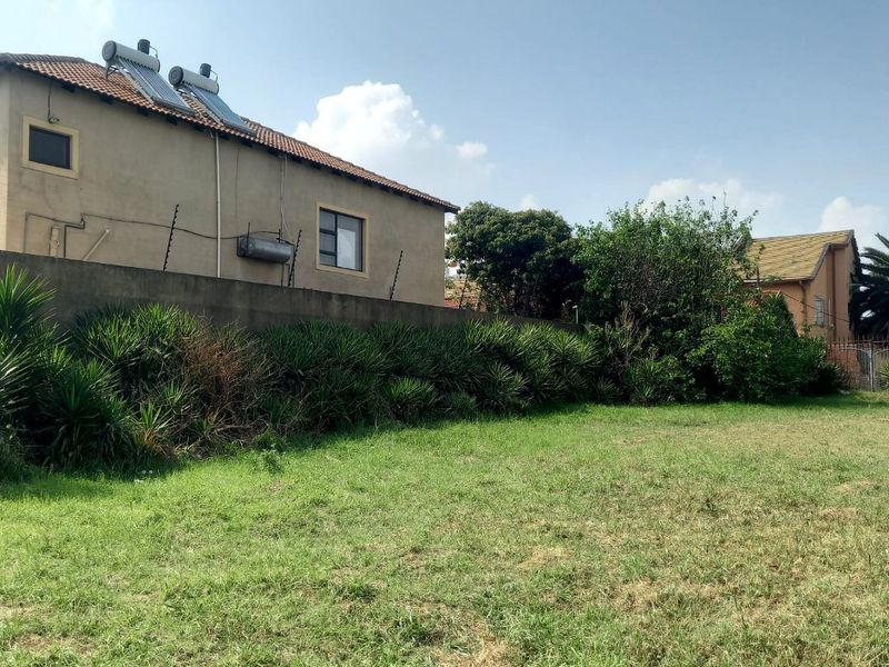 A view of the rear yard featuring a grass lawn, boundary wall with electric fencing, and a house with a solar water heating system.