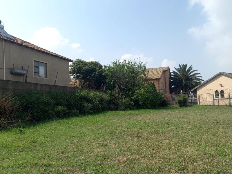 A view of a vacant residential plot featuring a grass lawn, boundary wall, and established perimeter electric fencing.