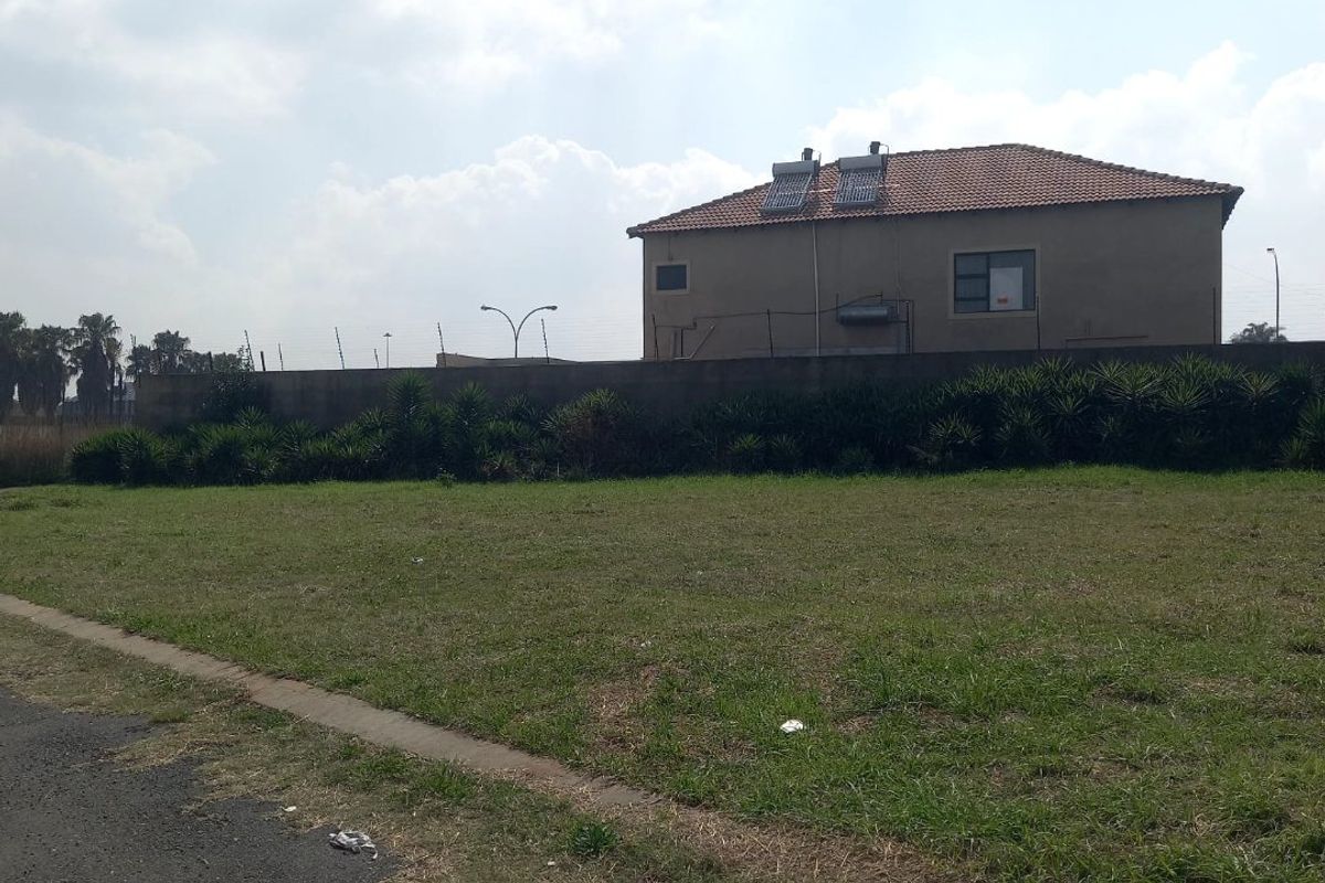 A view of the rear exterior of a residential property featuring a perimeter wall, tiled roof, and solar water heating system on a vacant lot.