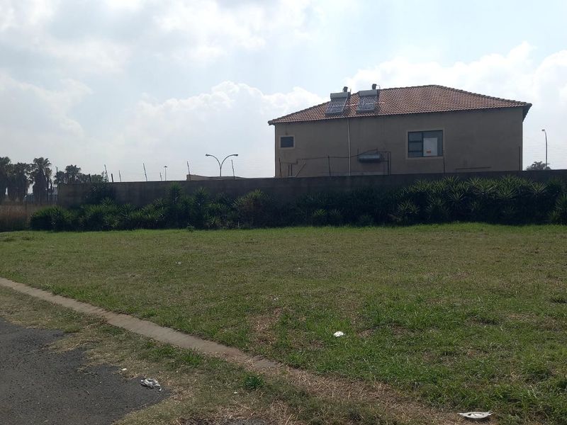 A view of the rear exterior of a residential property featuring a perimeter wall, tiled roof, and solar water heating system on a vacant lot.
