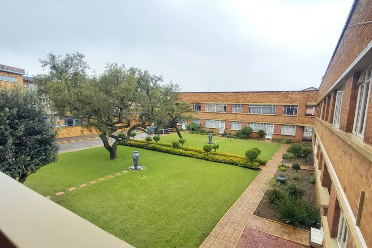 An elevated view of a communal garden area featuring a well-maintained lawn, paved pathways, and brick apartment building facades.