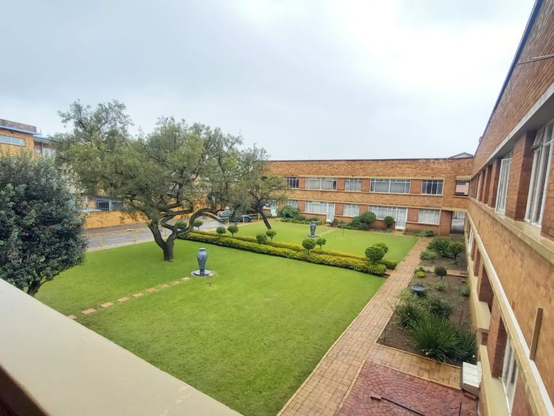 An elevated view of a communal garden area featuring a well-maintained lawn, paved pathways, and brick apartment building facades.