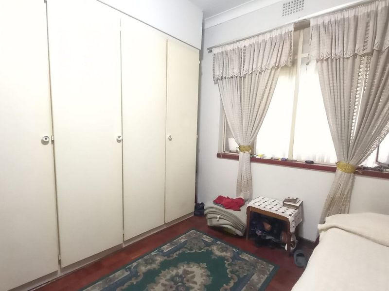 A bedroom featuring timber-look flooring, a large built-in wardrobe, and a window with natural light.
