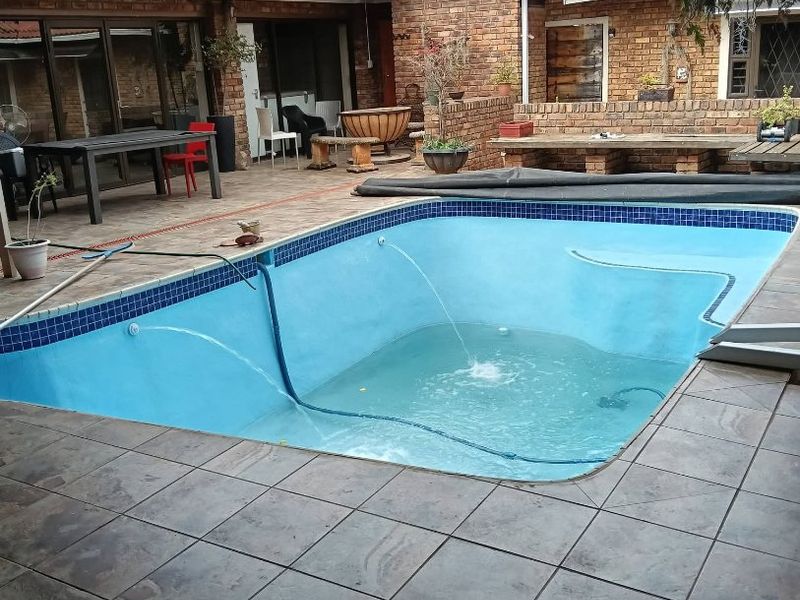 Outdoor entertainment area featuring a swimming pool, tiled patio, and brick-built seating, set against a face-brick house exterior.