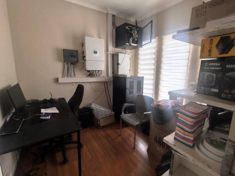 A utility room featuring a solar inverter, electrical distribution board, and network infrastructure, currently utilized as a home office and storage area.