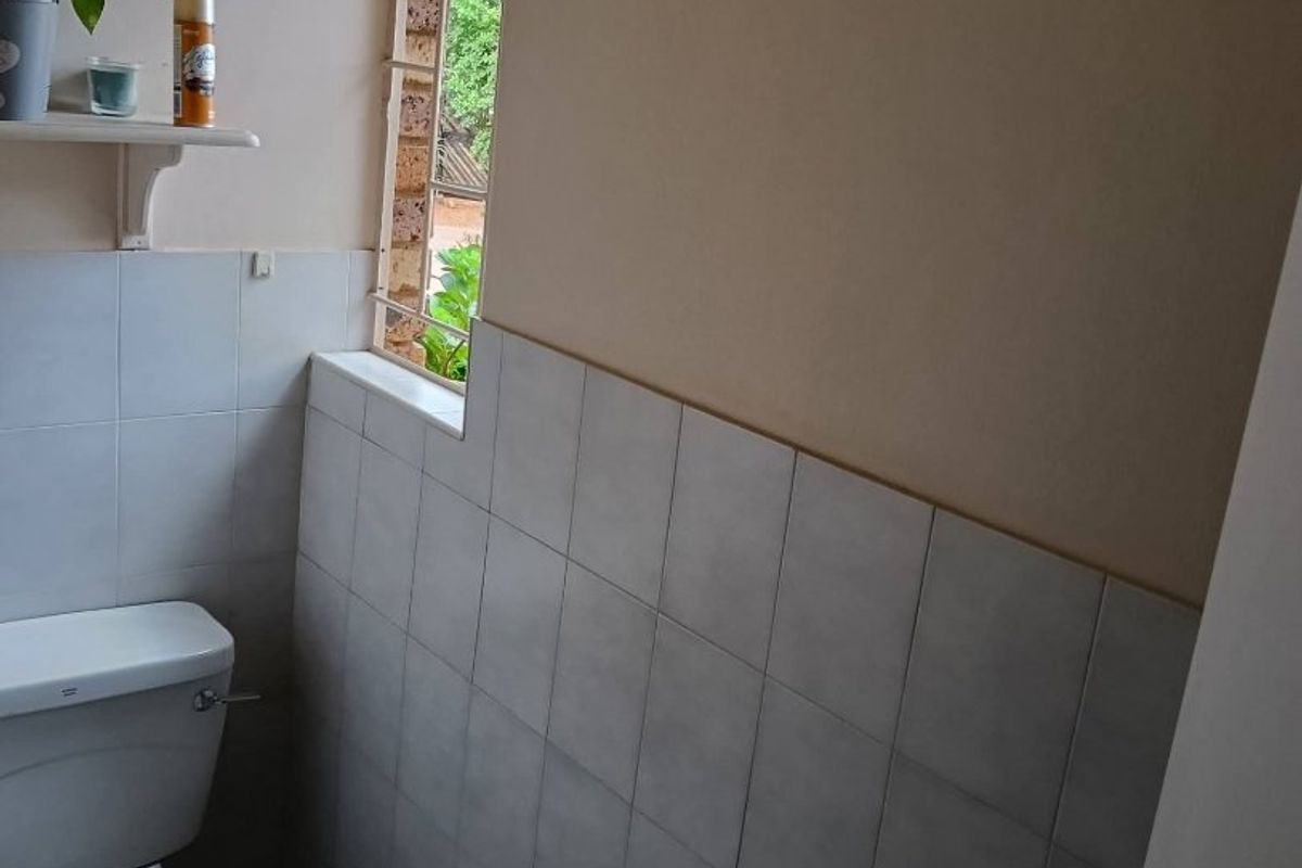 A compact bathroom featuring a standard toilet, partial wall tiling, and a window with security bars.