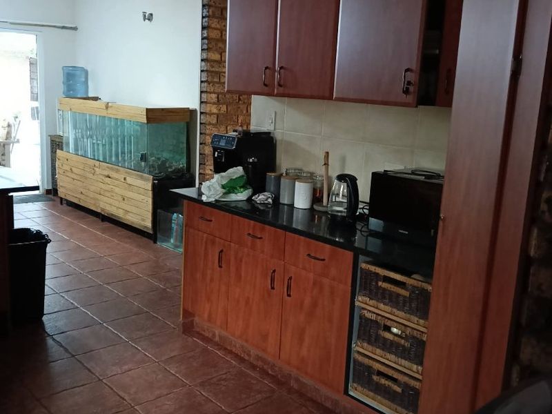 Kitchen area featuring dark wood cabinetry, granite countertops, and terracotta-style floor tiles, complemented by an exposed brick feature pillar.