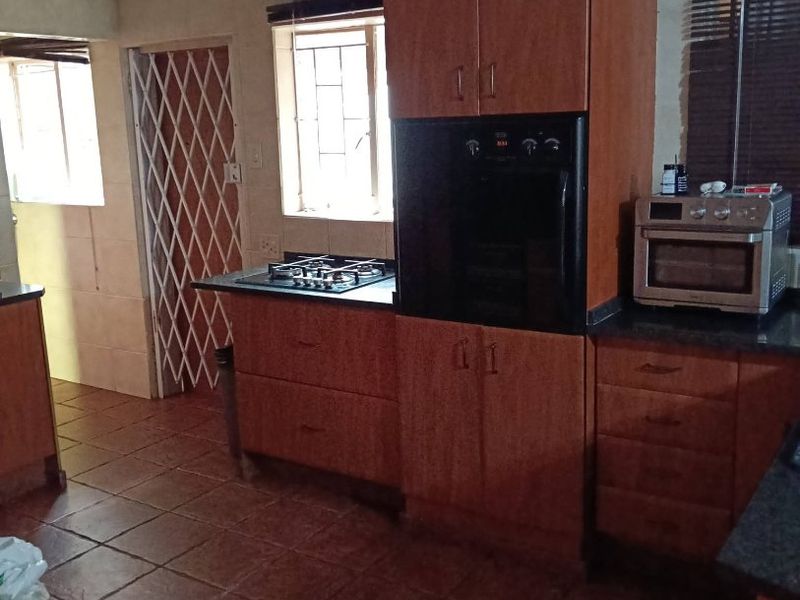 A functional kitchen featuring wooden cabinetry, built-in oven, gas hob, extractor fan, and tiled flooring with direct access to an exterior security gate.