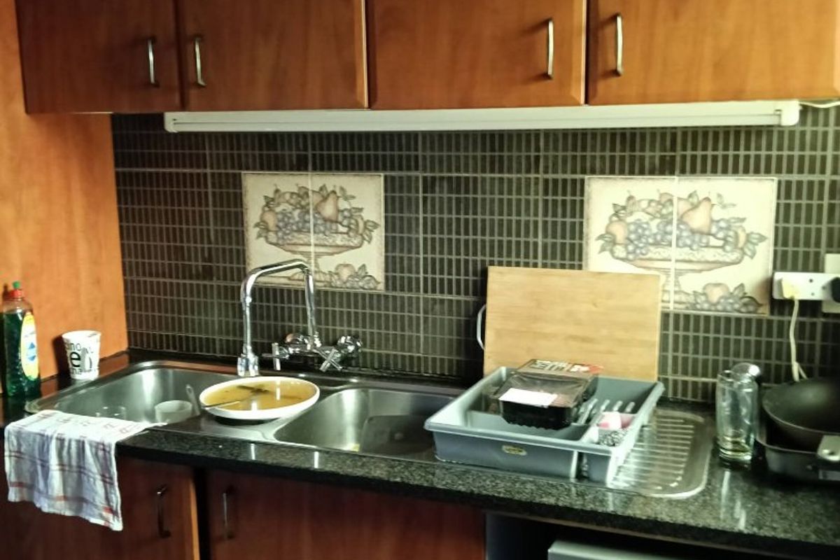 A functional kitchen area featuring wood-finish cabinetry, granite countertops, a double stainless steel sink, and a tiled splashback with decorative accents.