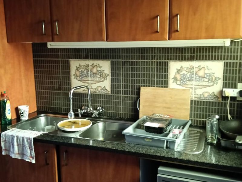 A functional kitchen area featuring wood-finish cabinetry, granite countertops, a double stainless steel sink, and a tiled splashback with decorative accents.