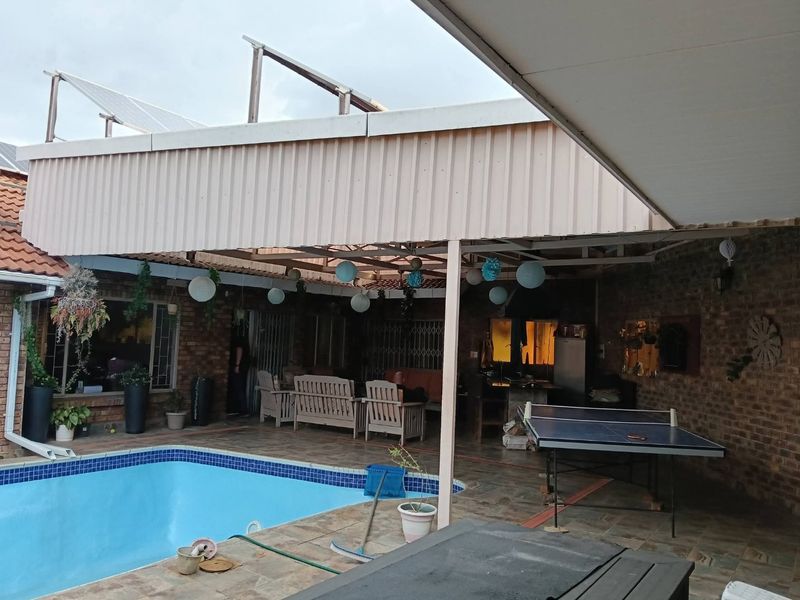 Covered outdoor patio area featuring a built-in braai, tiled flooring, and direct access to the adjacent swimming pool.