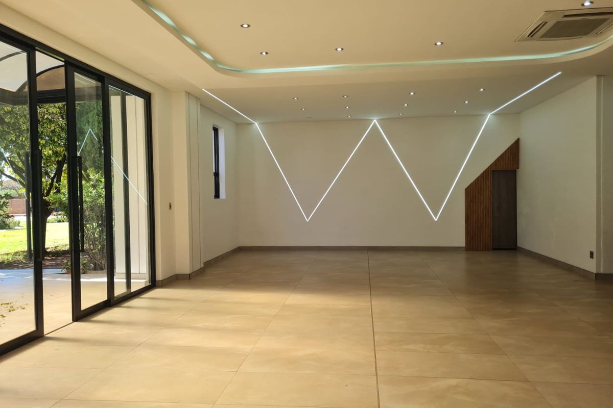 A spacious, modern open-plan area featuring large format floor tiles, contemporary LED wall lighting, and expansive sliding glass doors leading to the garden.