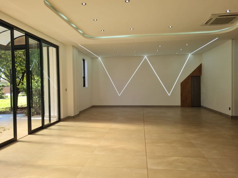 A spacious, modern open-plan area featuring large format floor tiles, contemporary LED wall lighting, and expansive sliding glass doors leading to the garden.