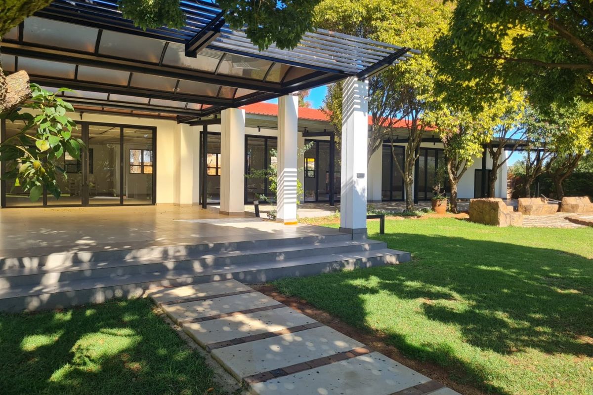 A spacious covered patio area featuring a modern pergola, concrete steps, and direct access to the building through large sliding glass doors.