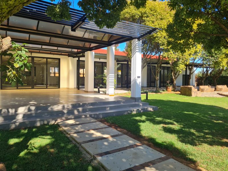 A spacious covered patio area featuring a modern pergola, concrete steps, and direct access to the building through large sliding glass doors.