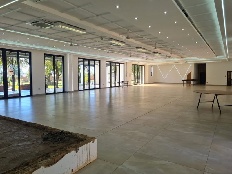 Spacious open-plan commercial area featuring large glass sliding doors, modern recessed ceiling lighting, and tiled flooring, suitable for events or office use.