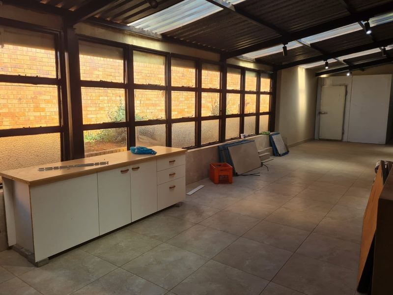 A spacious utility area featuring tiled flooring, extensive natural light through metal-framed windows, translucent roof panels, and built-in storage cabinetry.