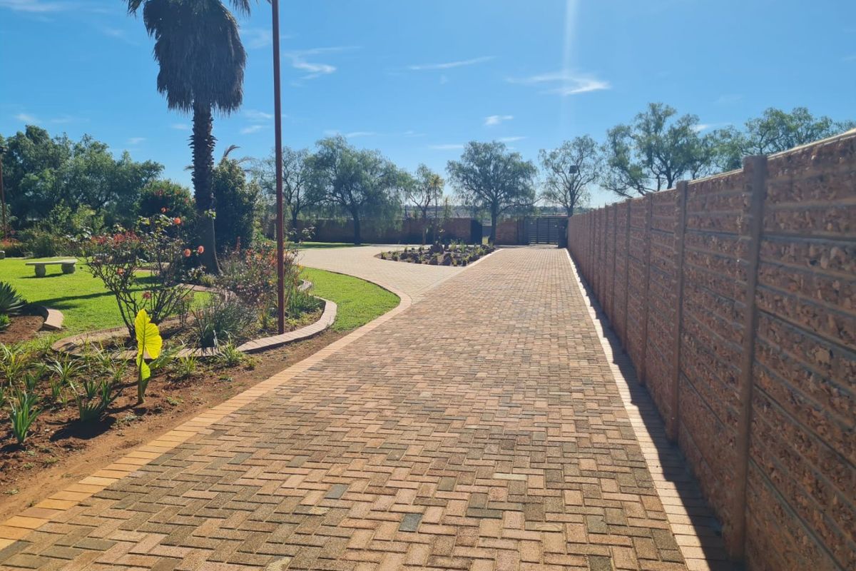 A well-maintained paved driveway leading through a landscaped garden, bordered by a sturdy precast concrete boundary wall.