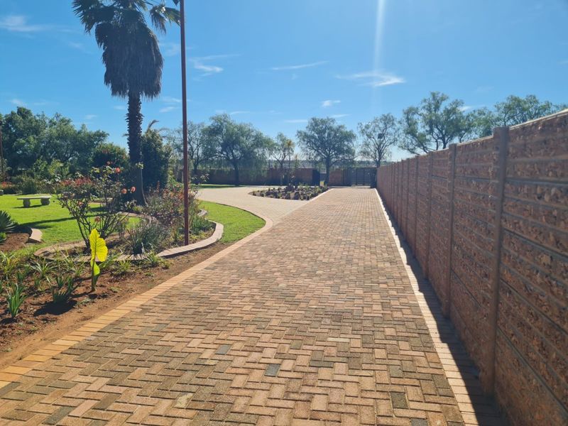 A well-maintained paved driveway leading through a landscaped garden, bordered by a sturdy precast concrete boundary wall.