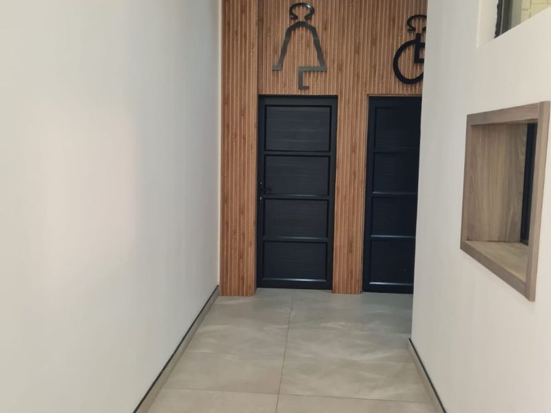 A clean, modern hallway featuring tiled flooring, timber slat wall accents, and clearly marked restroom access points.