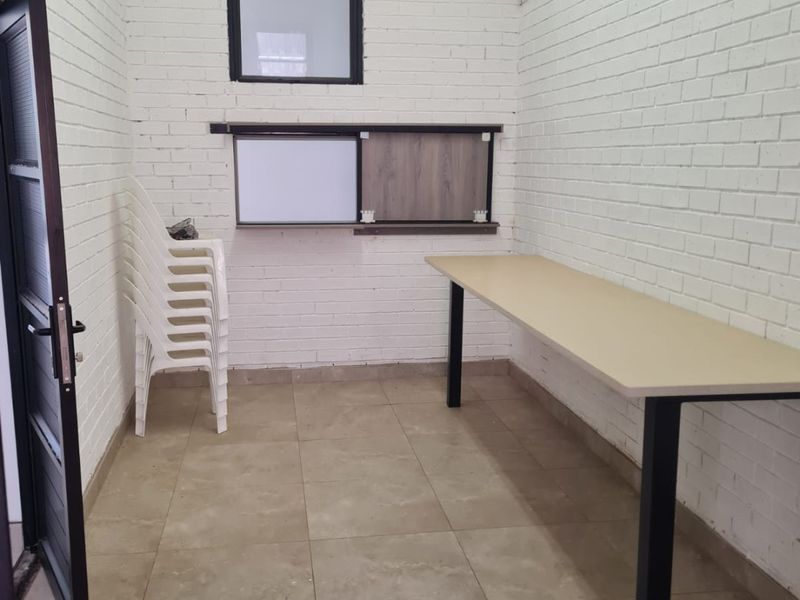 A functional office or utility space featuring painted brick walls, tiled flooring, a fixed desk, and a sliding service window.