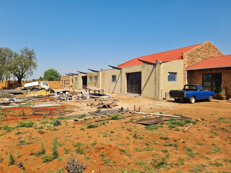 Rear view of a commercial property under construction, featuring a brick and plastered facade with a red corrugated metal roof.