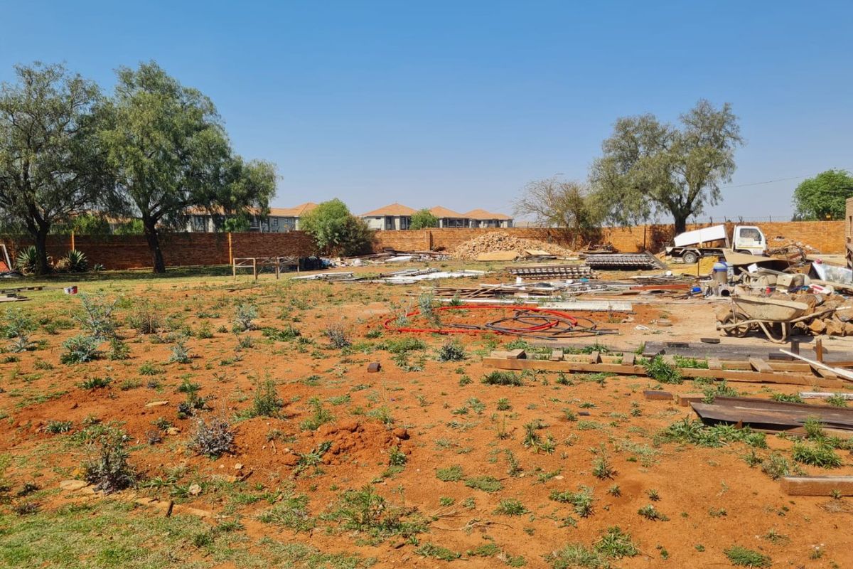 A large, undeveloped commercial plot featuring a brick perimeter wall and open land, currently used for storage of construction materials.