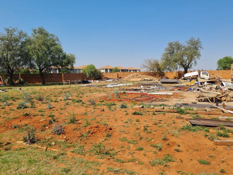 A large, undeveloped commercial plot featuring a brick perimeter wall and open land, currently used for storage of construction materials.