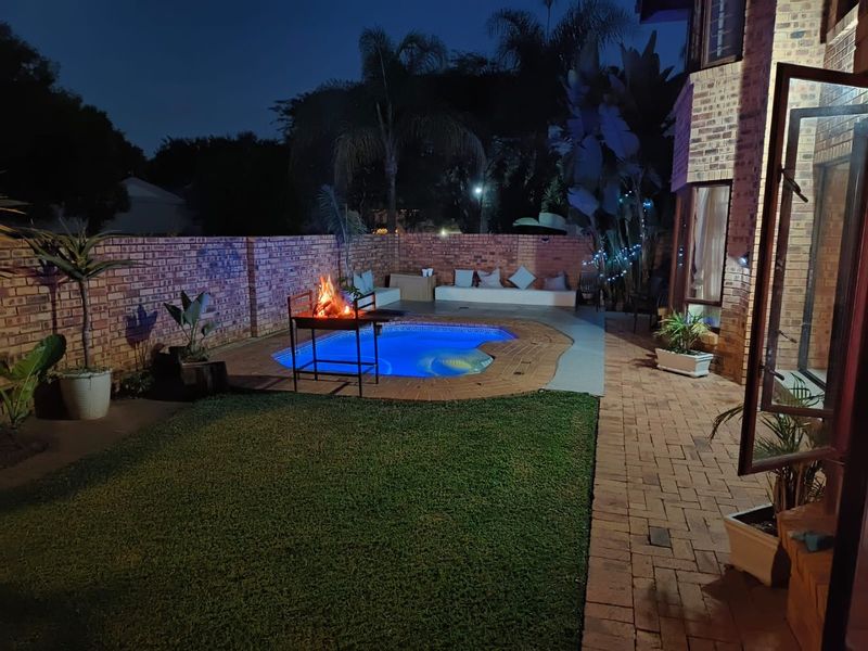 Night view of a private backyard featuring a swimming pool, paved patio area, and built-in bench seating against a brick boundary wall.