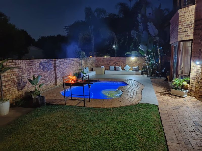 Night view of a private backyard featuring a swimming pool, brick paved surround, and built-in seating area, perfect for outdoor entertaining.