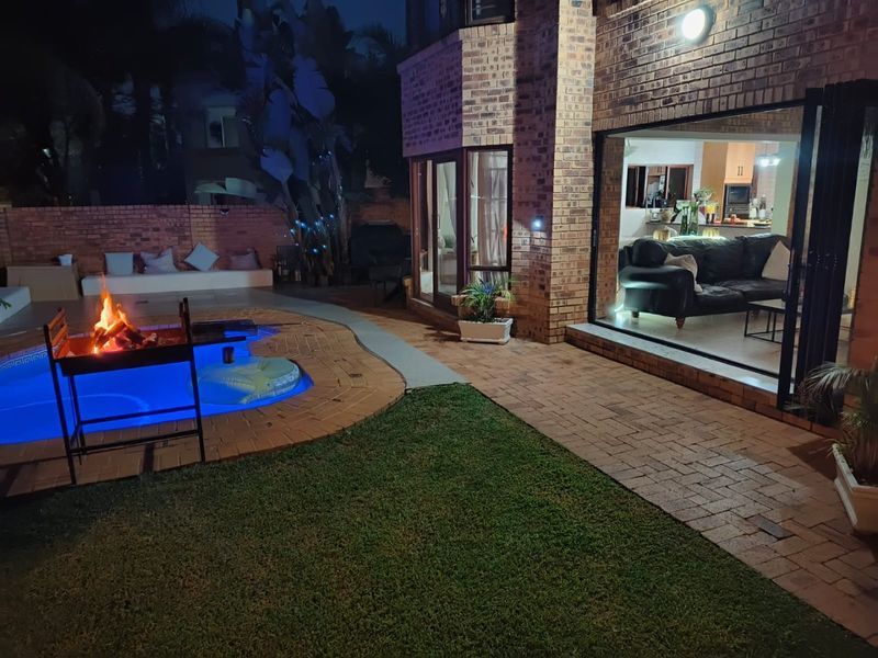 Night view of a rear garden featuring a swimming pool, brick patio, and seamless indoor-outdoor flow through large stacking doors into the living area.