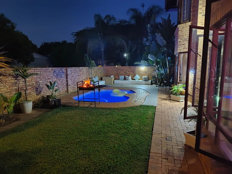Night view of a private backyard featuring a swimming pool, paved patio area, and brick boundary wall, ideal for outdoor entertaining.
