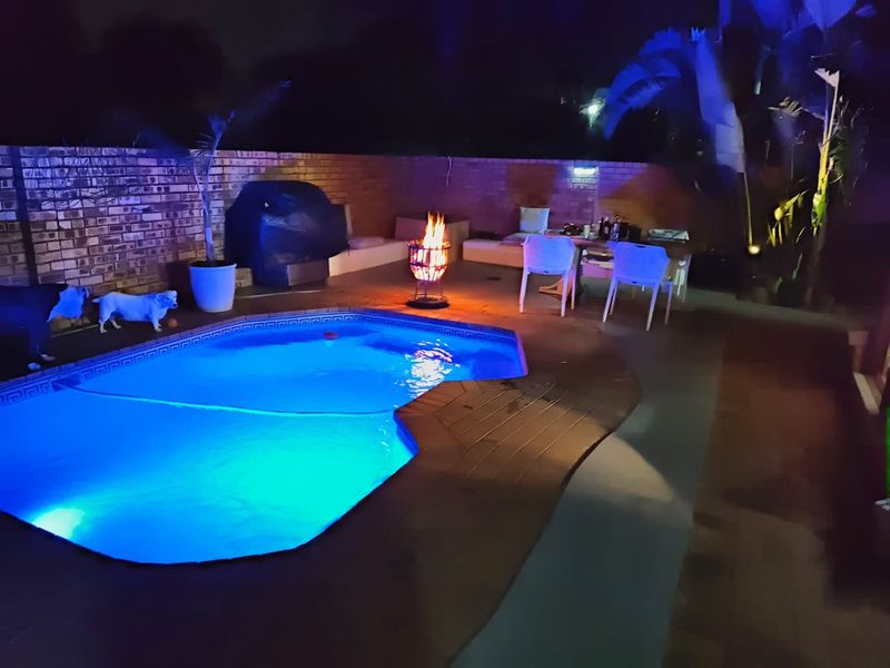 Nighttime view of a backyard swimming pool area featuring a paved surround and brick boundary wall.