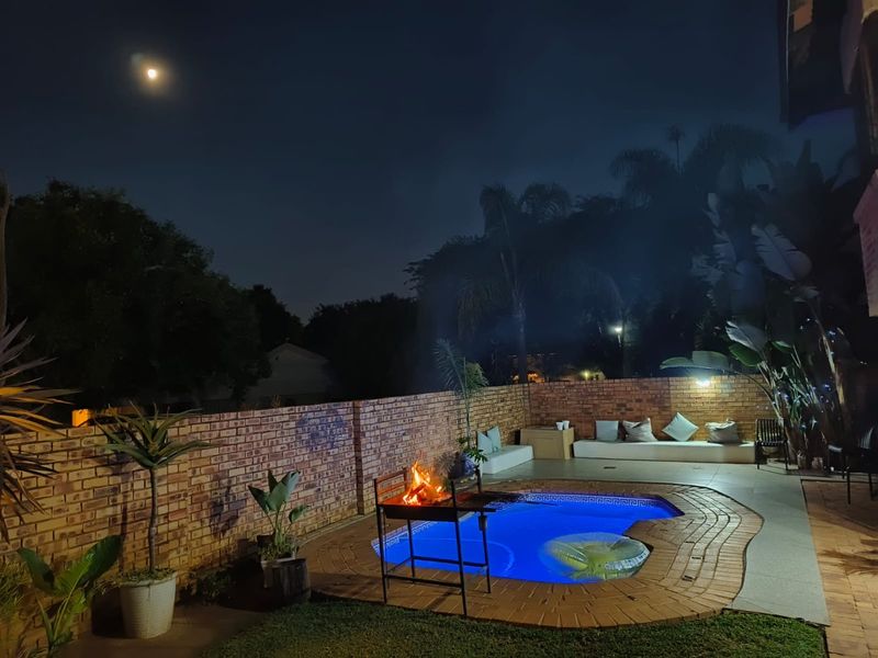 Night view of a private swimming pool area featuring a paved surround, brick boundary wall, and built-in outdoor seating.