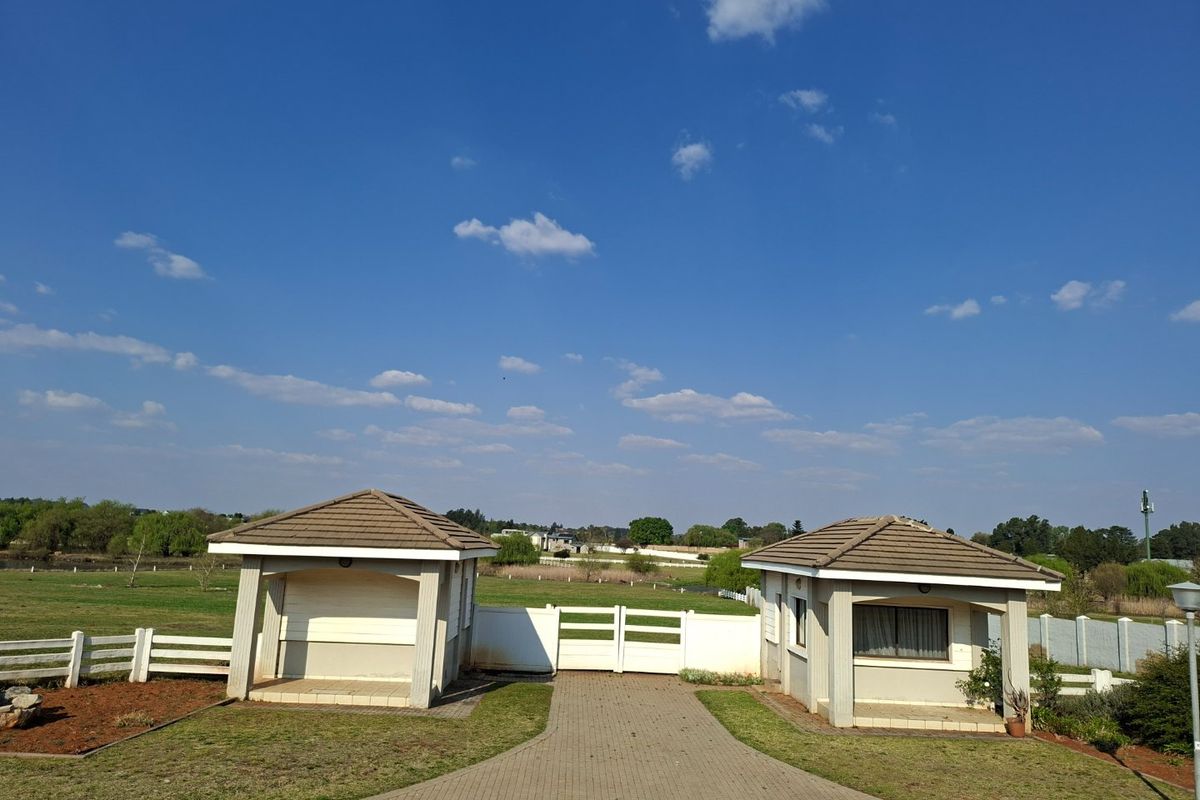 A well-maintained gated entrance featuring two guard houses with tiled roofs, a paved driveway, and perimeter fencing set within a spacious residential land area.