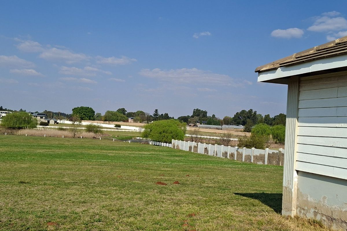 A view of the rear yard featuring a large grassy area, precast concrete boundary wall, and a section of the existing residential structure.