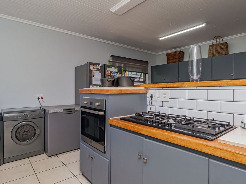 A functional kitchen featuring grey cabinetry, timber countertops, a gas hob, built-in oven, and a classic subway tile backsplash.