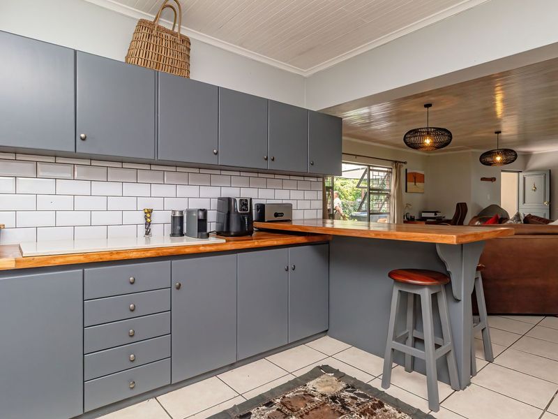 Open-plan kitchen featuring modern grey cabinetry, timber countertops, subway tile backsplash, and a breakfast bar, seamlessly flowing into the adjacent living area.