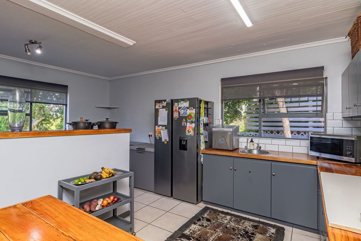 A functional kitchen featuring grey cabinetry, timber countertops, subway tile backsplash, and tiled flooring, offering a clean and practical workspace.