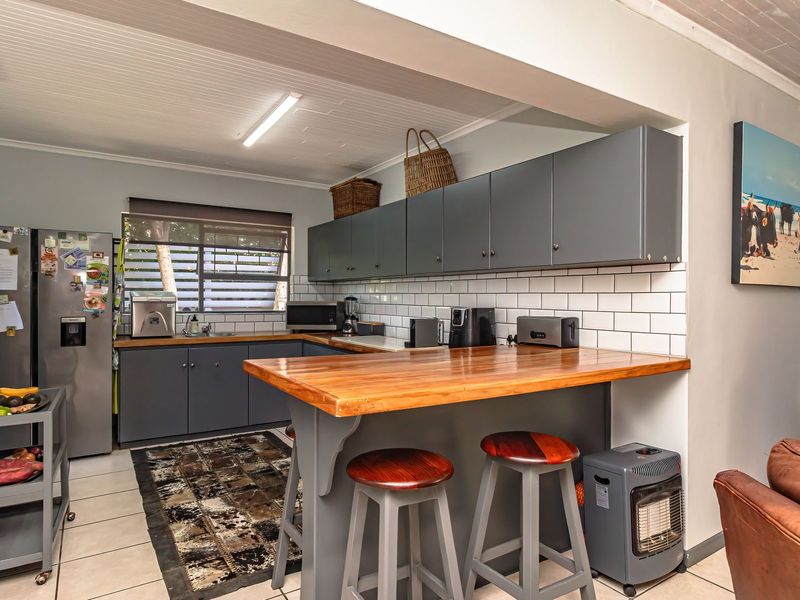 Open plan kitchen featuring grey cabinetry, subway tile backsplash, and a timber breakfast bar, seamlessly integrated with the living area.