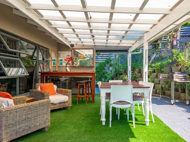Covered outdoor patio area featuring a pergola with translucent roofing, artificial turf, and a tiered garden retaining wall, ideal for alfresco dining and entertaining.