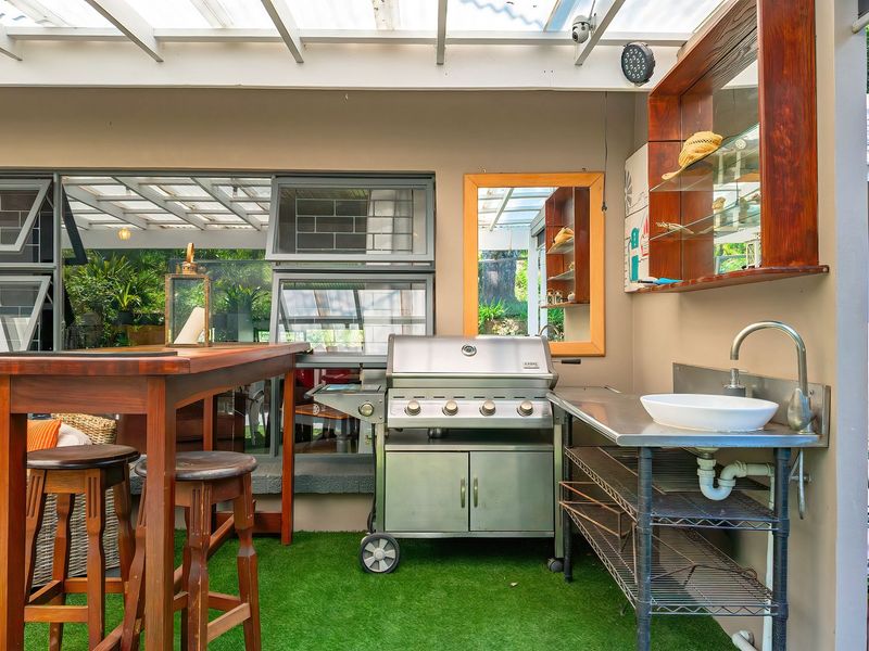 Covered outdoor patio area featuring a built-in sink, shelving, and space for a barbecue, ideal for alfresco dining and entertaining.