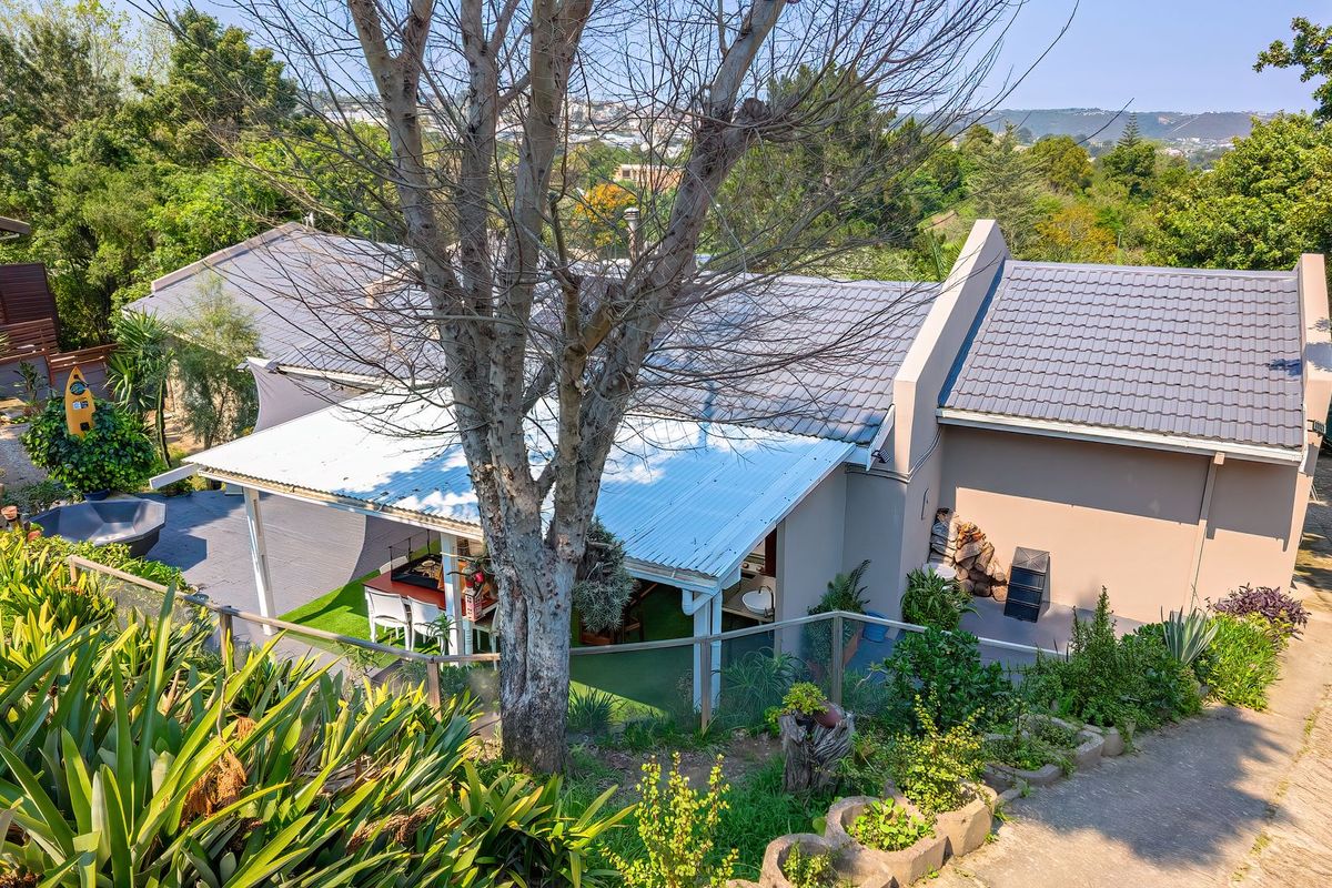 Elevated view of the rear exterior featuring a tiled roof, a covered patio area, and a landscaped garden with a concrete driveway.