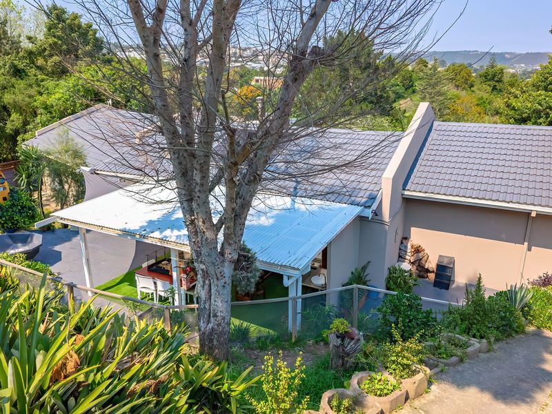 Elevated view of the rear exterior featuring a tiled roof, a covered patio area, and a landscaped garden with a concrete driveway.