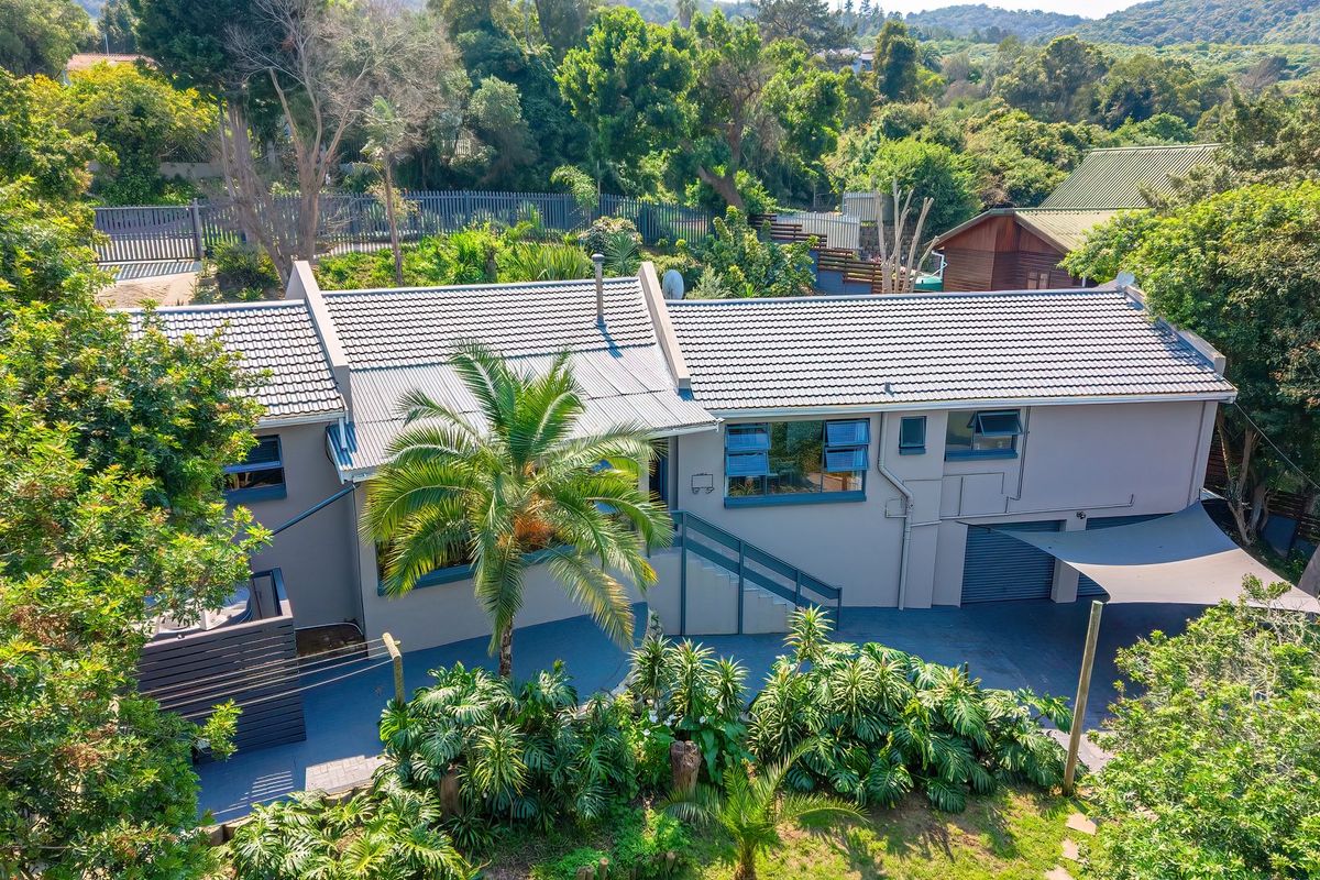 Aerial view of a well-maintained residential property featuring a tiled roof, paved driveway, garage, and established garden surroundings.