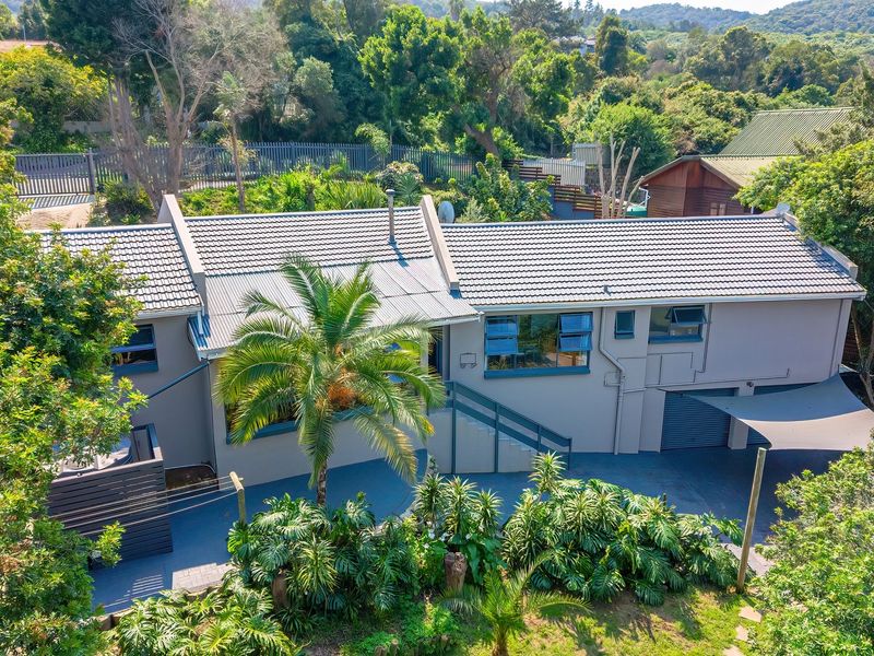 Aerial view of a well-maintained residential property featuring a tiled roof, paved driveway, garage, and established garden surroundings.