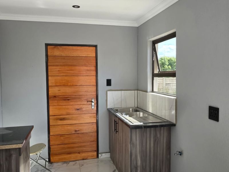 A compact kitchen area featuring modern marble-look floor tiles, wood-grain cabinetry, a stainless steel sink, and a solid timber door.
